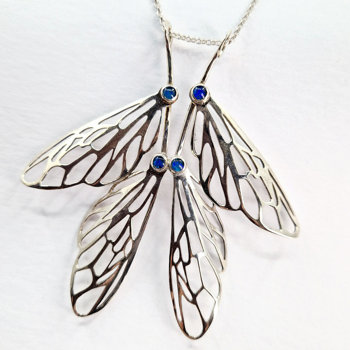 Butterfly wing-shaped pendant with blue gemstones on a white background