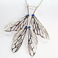 Butterfly wing-shaped pendant with blue gemstones on a white background