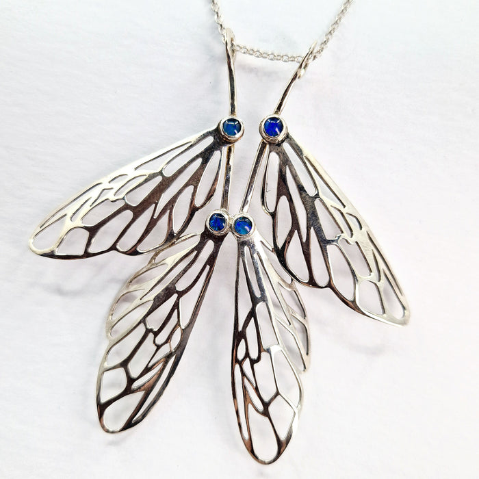 Butterfly wing-shaped pendant with blue gemstones on a white background