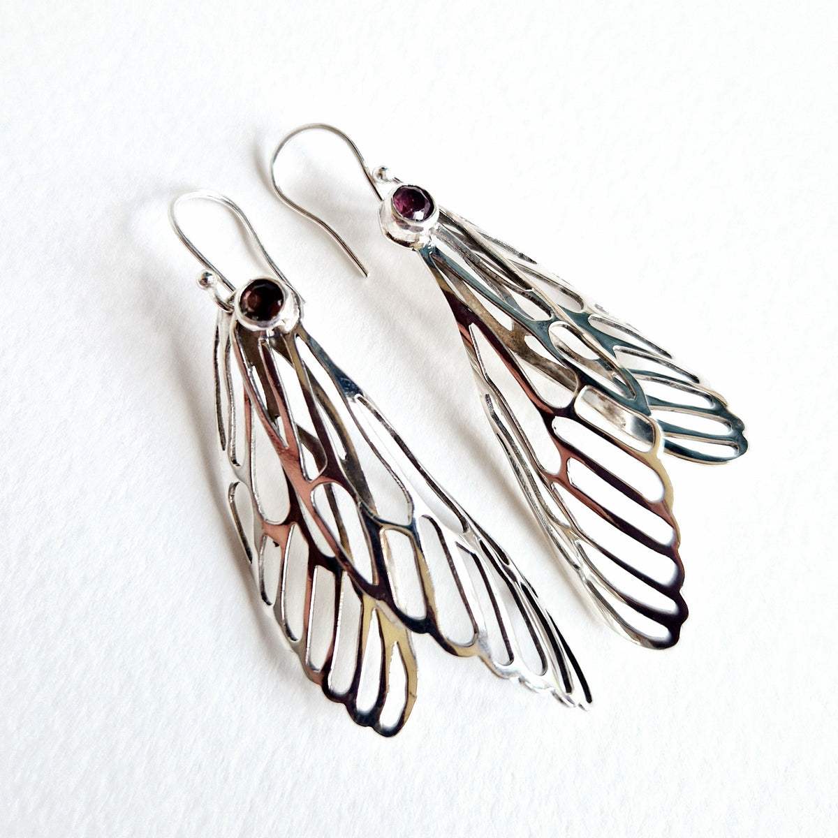 Silver wing-shaped earrings with gemstones on a white background