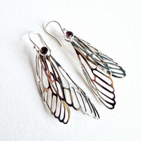Silver wing-shaped earrings with gemstones on a white background