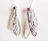Silver wing-shaped earrings with red gemstones on a white background