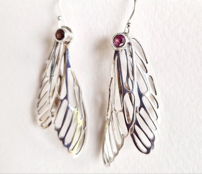 Silver wing-shaped earrings with red gemstones on a white background