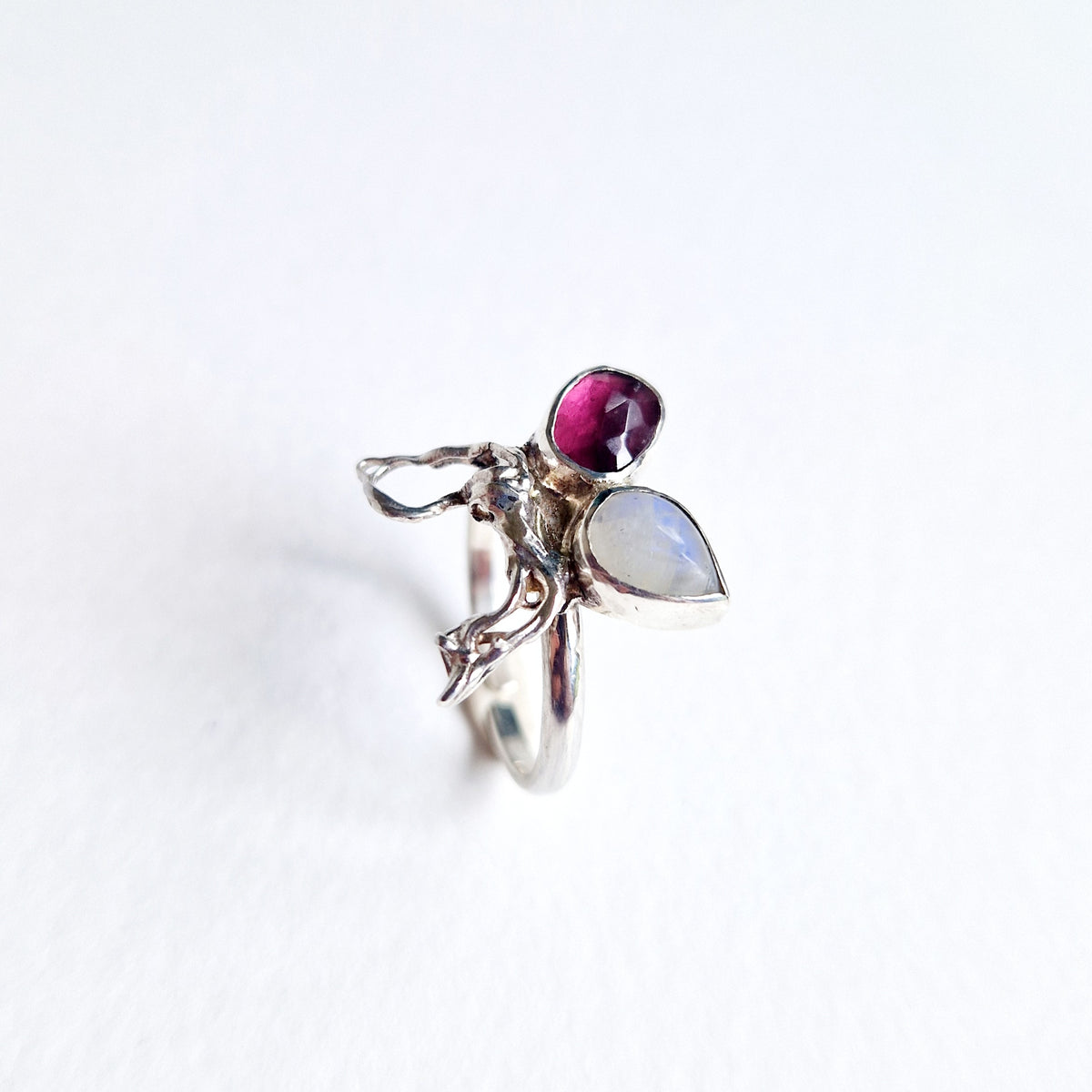 Silver ring with a purple gemstone and a teardrop-shaped moonstone on a white background