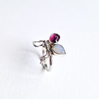 Silver ring with a purple gemstone and a teardrop-shaped moonstone on a white background