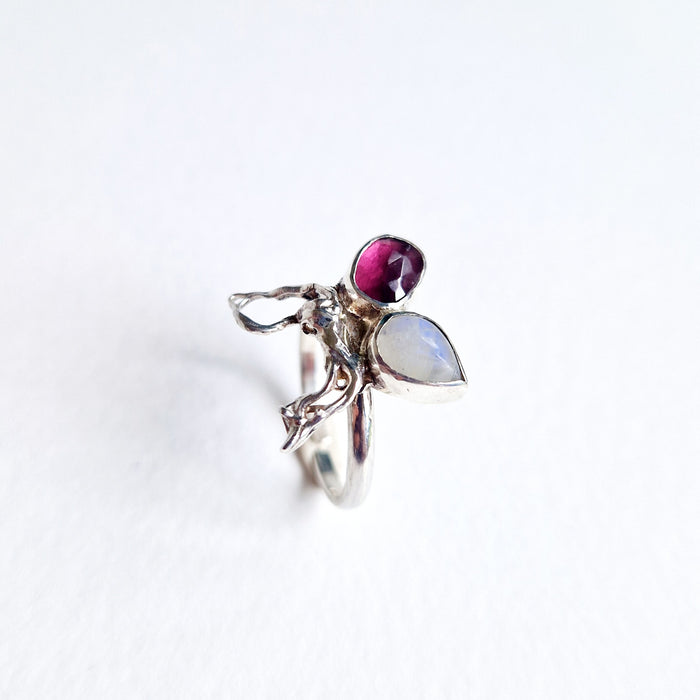 Silver ring with a purple gemstone and a teardrop-shaped moonstone on a white background