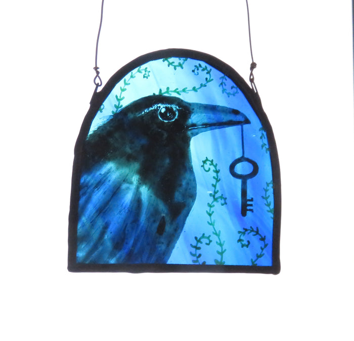 Stained glass panel with a raven and key design on a blue background