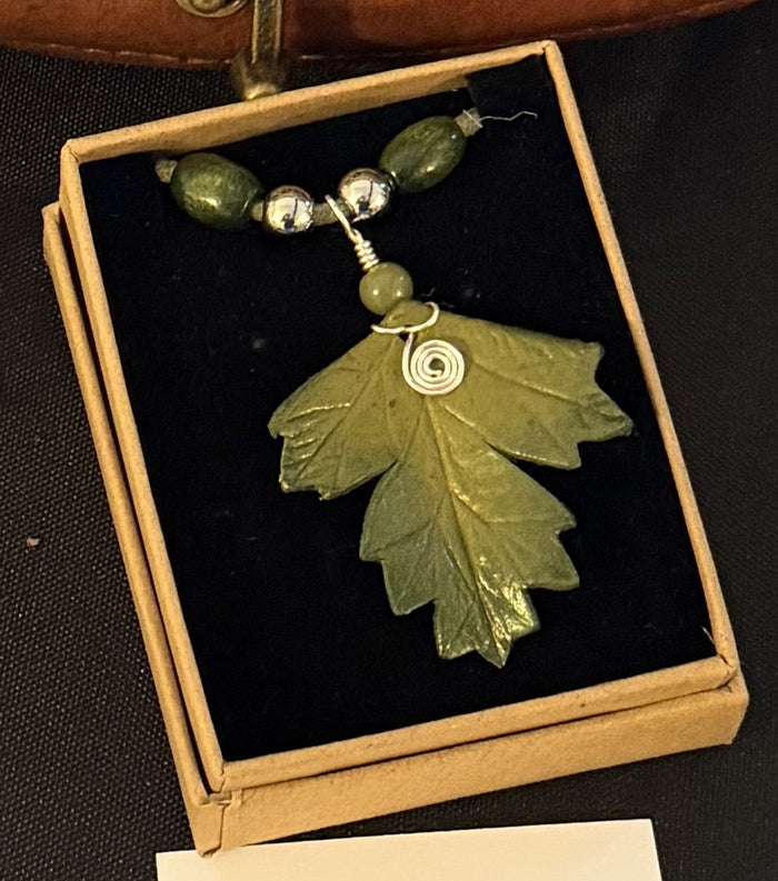 Green leaf-shaped pendant with beads in a box on a dark surface