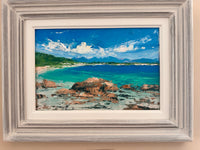 Framed painting of a coastal scene with rocks, water, and sky.