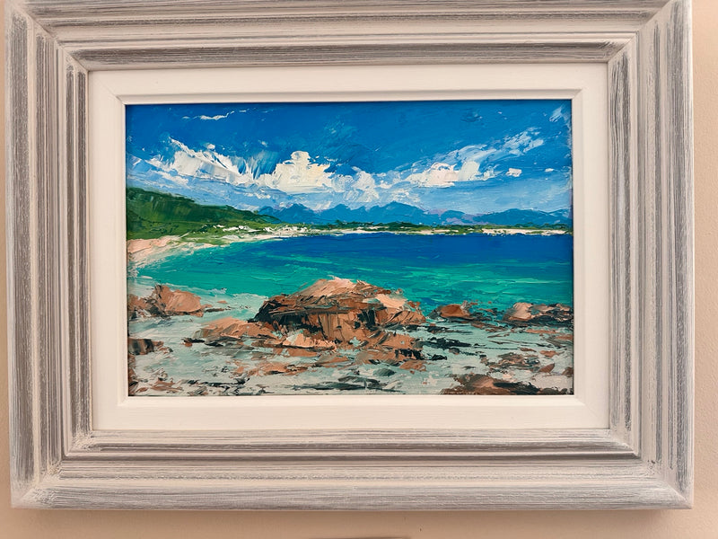 Framed painting of a coastal scene with rocks, water, and sky.