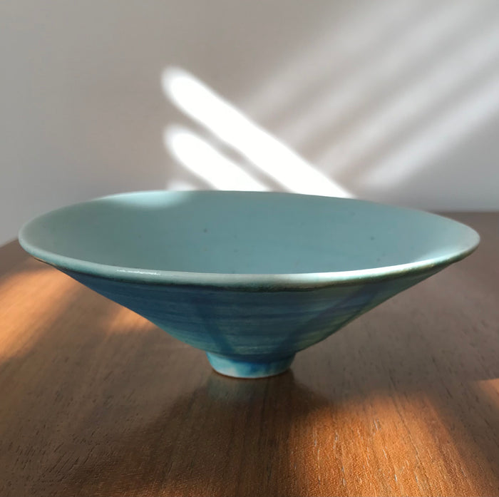Blue ceramic bowl on a wooden surface with sunlight casting shadows