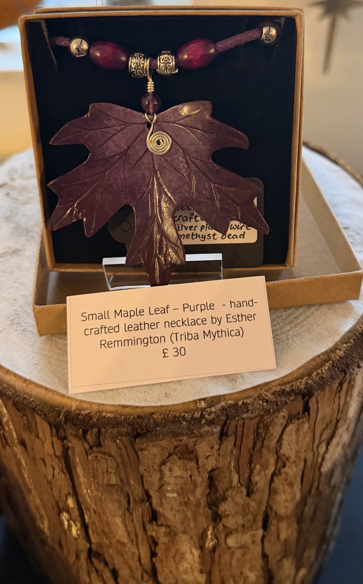 Purple leaf-shaped necklace in a box with a label on a wooden surface