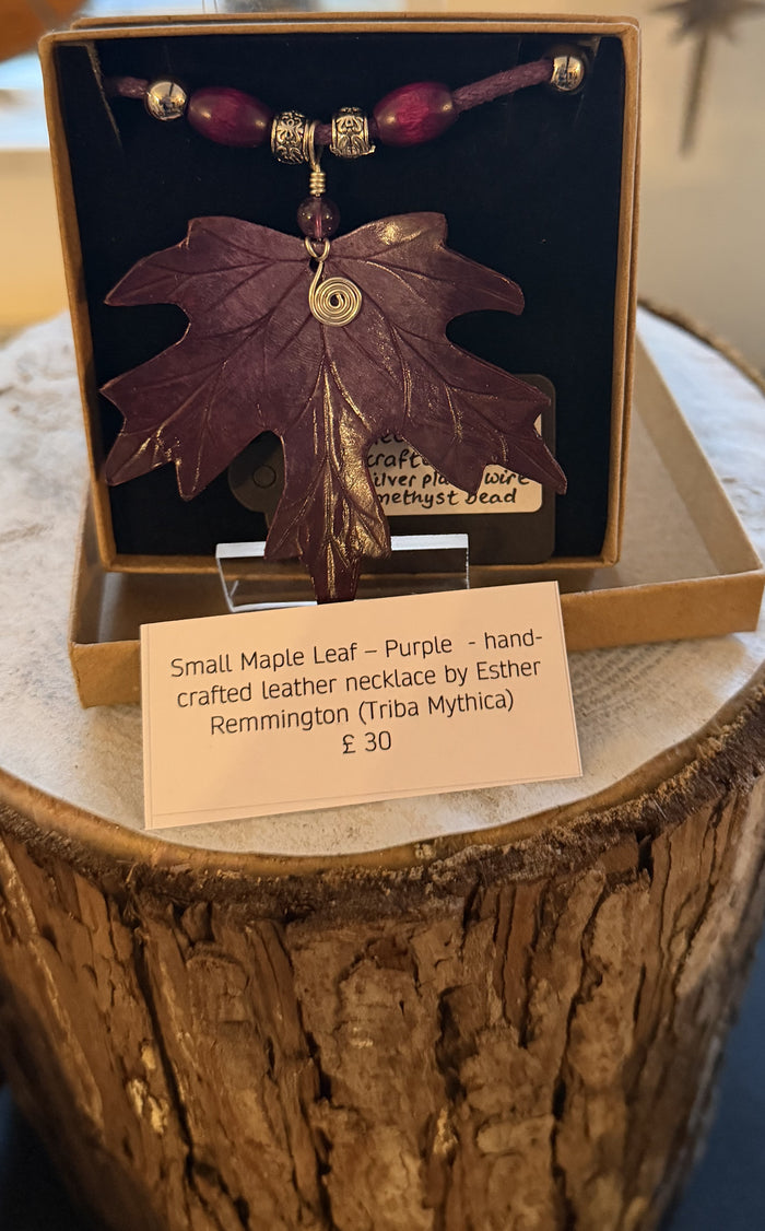 Purple leaf-shaped necklace in a box with a label on a wooden surface